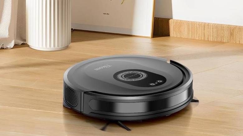 A black Tikom robot vacuum on the floor of a house