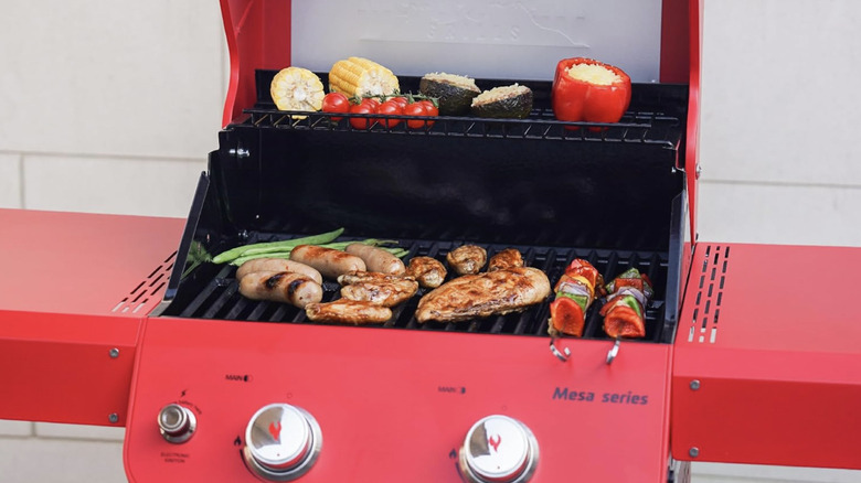 Mesa grill in red color with various foods cooking on the surface