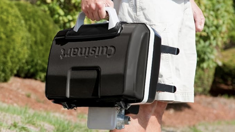 Black Cuisinart tabletop stove with handle being carried by a man outside