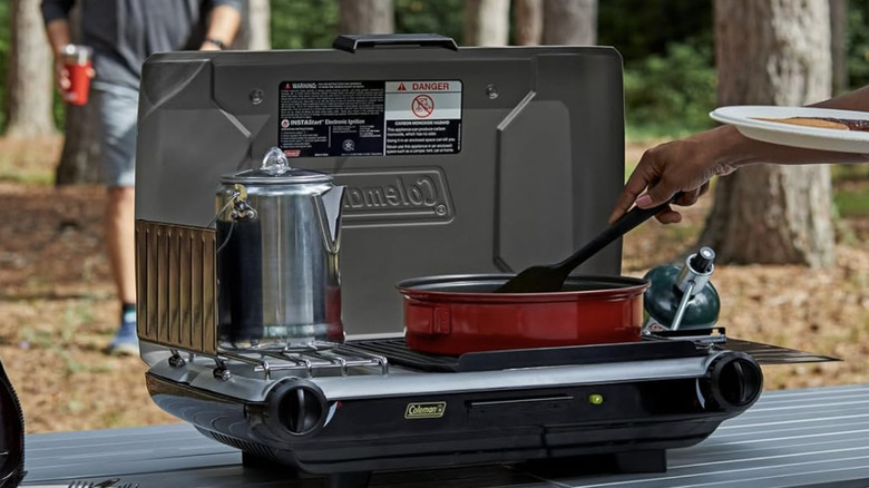 Tabletop stove being used in nature to cook and warm a kettle