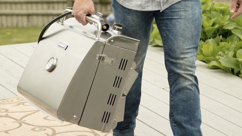Man holding a stainless steel grill by handle and walking on a porch