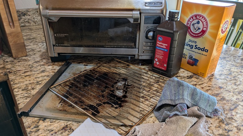 A toaster oven with crumb tray and rack removed next to cleaning supplies