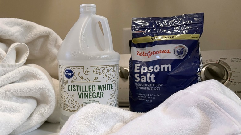 A large bag of Epsom salt and gallon of distilled white vinegar sit on a washing machine surrounded with towels