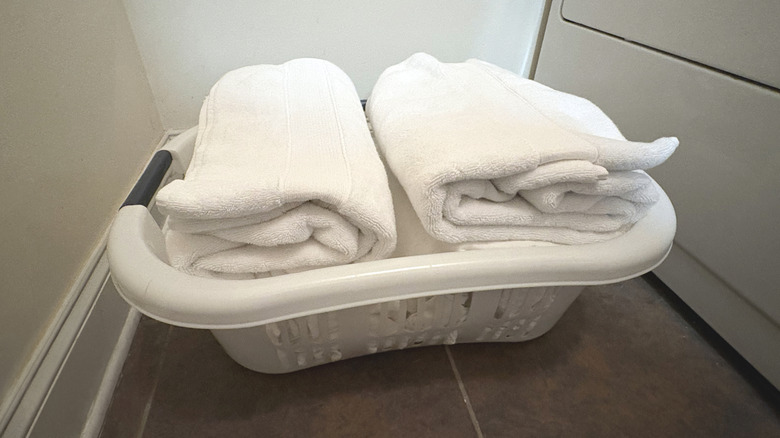 A white laundry baskets filled with folded duvet covers and bath towels sits on a tile floor