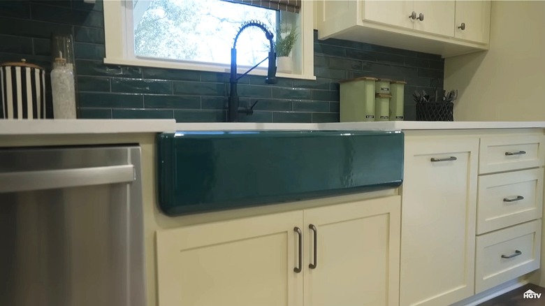 Kitchen farmhouse sink in a teal color, framed by cream cabinets and a white countertop.