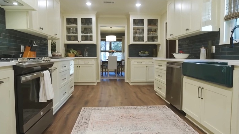 View of kitchen with teal porcelain sink inserted in cream cabinets. Counterop is white and backsplash is made of subway tiles in the same color as sink.
