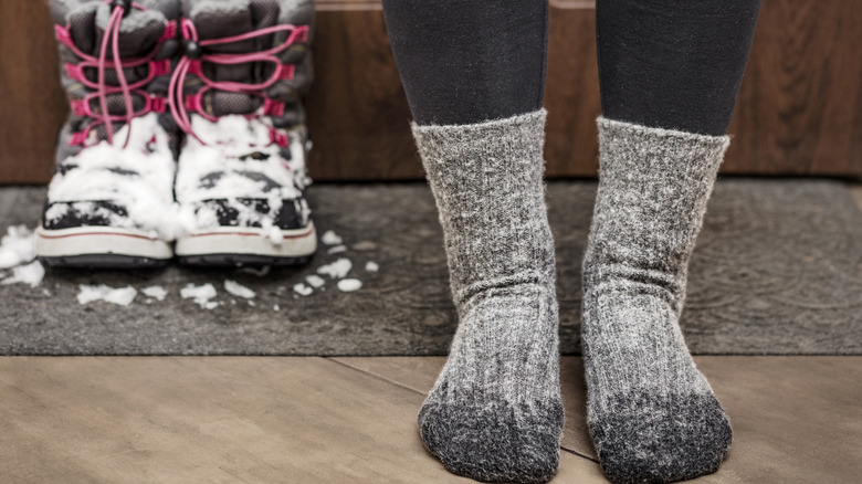 A person wearing wet wool socks with snow boots in the background covered in snow