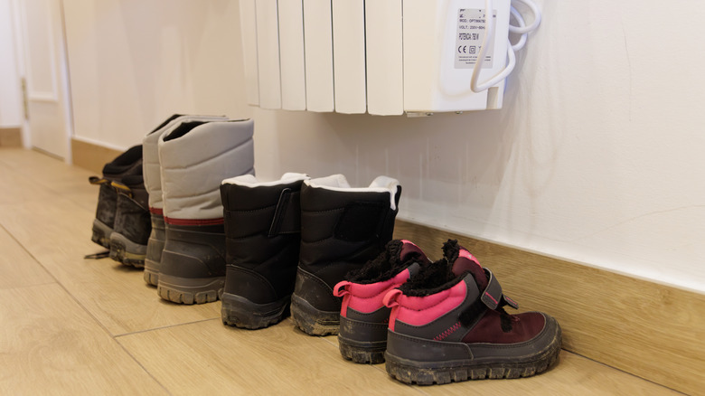 A series of shoes underneath a radiator, but not directly touching it, to dry.