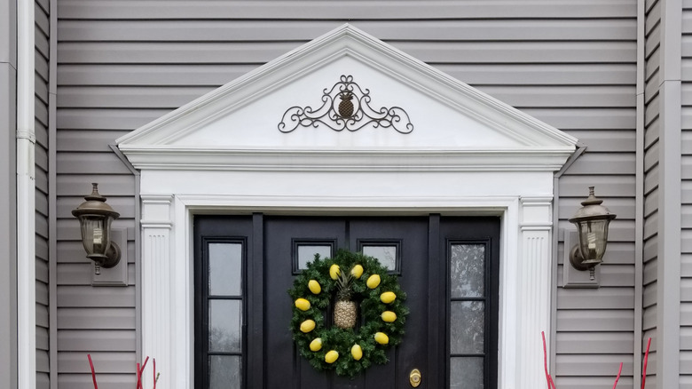 A close look at a front porch that has a pineapple-themed wreath and a pineapple door sign.