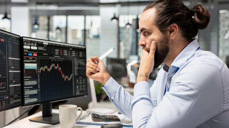 A day trader looks concerned while watching stock prices fall on his computer screens