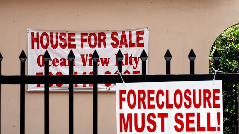 Signs reading "House for Sale" and "Foreclosure Must Sell!" hang near a peach stucco house