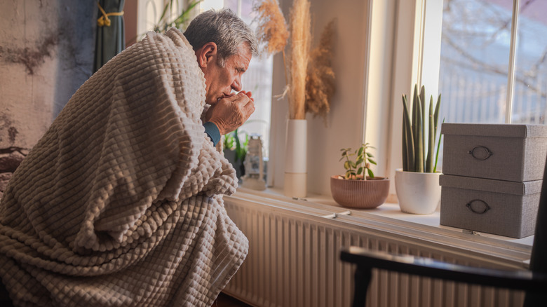 A man shivers under a blanket in front of an old radiator
