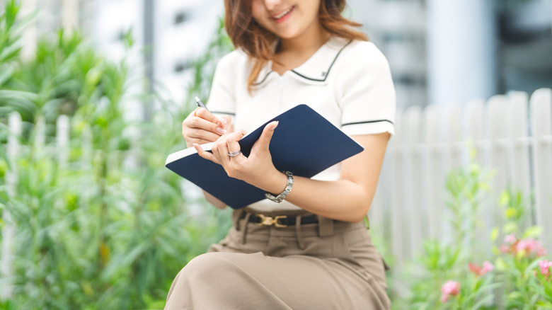 A woman takes notes in a notebook while in her garden.