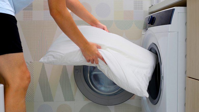 person putting pillow in washer