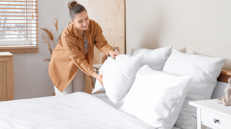 smiling person fluffing pillows on bed