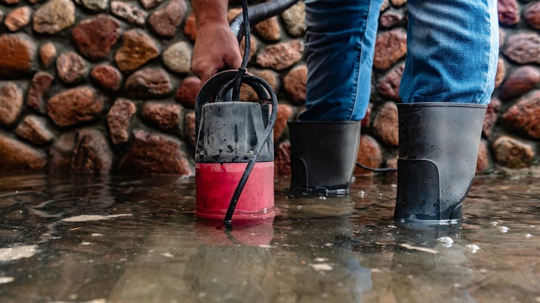 Flood water is being pumped out of a cobblestone basement by someone in thick rain boots.