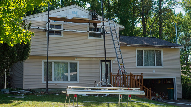 A contractor fixing siding on a two story home