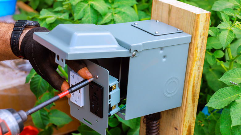 Person installing an outdoor electrical box in a garden