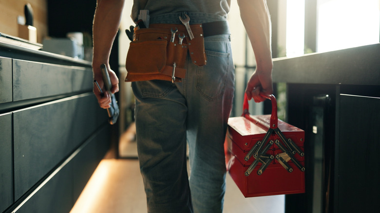Person walking in a kitchen holding a tool box