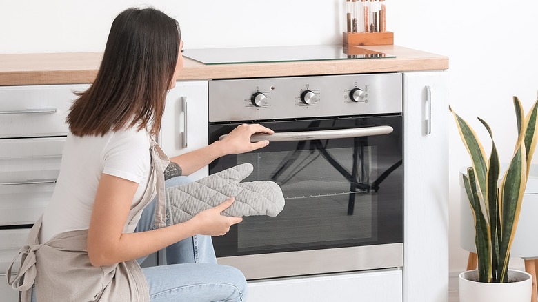 Person crouching, opening oven door