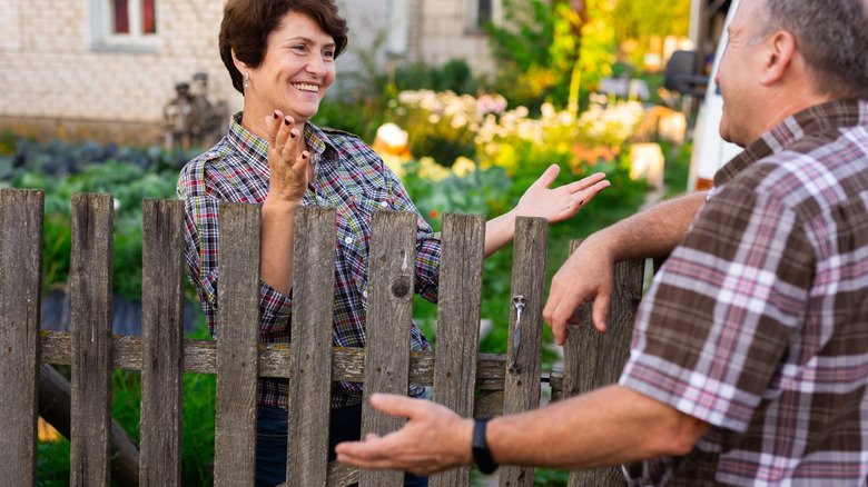 Two neighbors smiling and talking over a fence