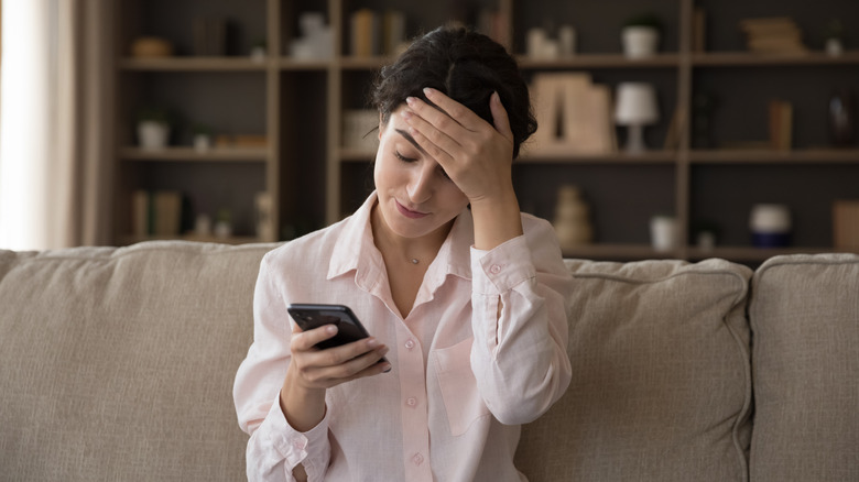 Frustrated woman sitting on couch looking at smart phone