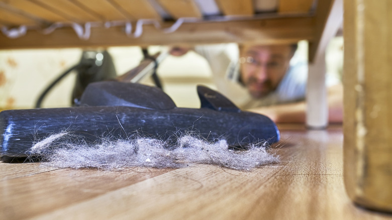 Man vacuuming up dust bunnies from under a bed