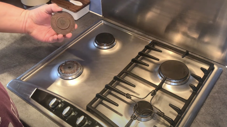 Person holding a burner cap above a gas stove