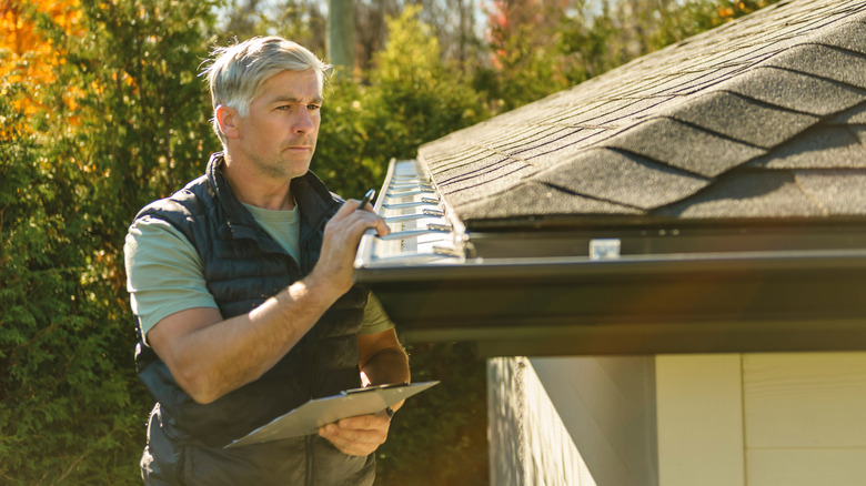 A man inspecting a home's roof with a cardboard in hand