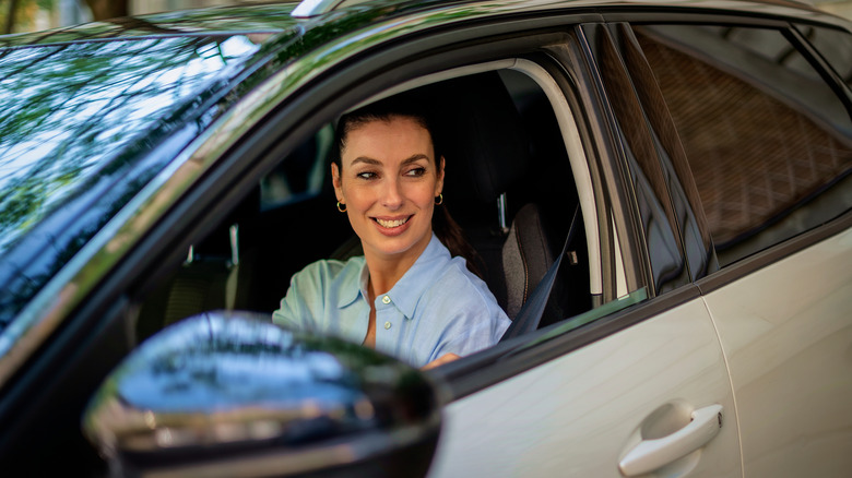 A smiling woman is looking out the window of a car