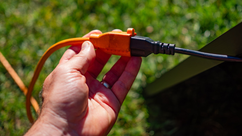 a person holding an orange extension cord with a black appliance cord plugged into it