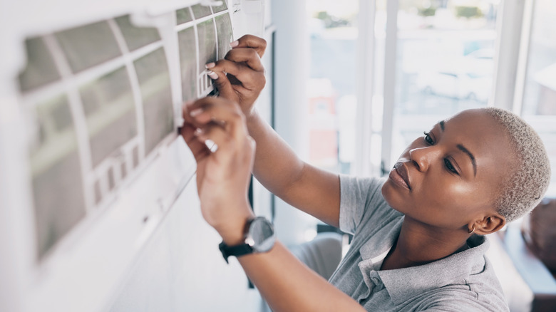 A short-haired African American woman fixes her wall-mounted AC unit.