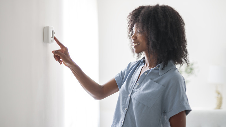 A woman adjusts the thermostat on the wall of her home.