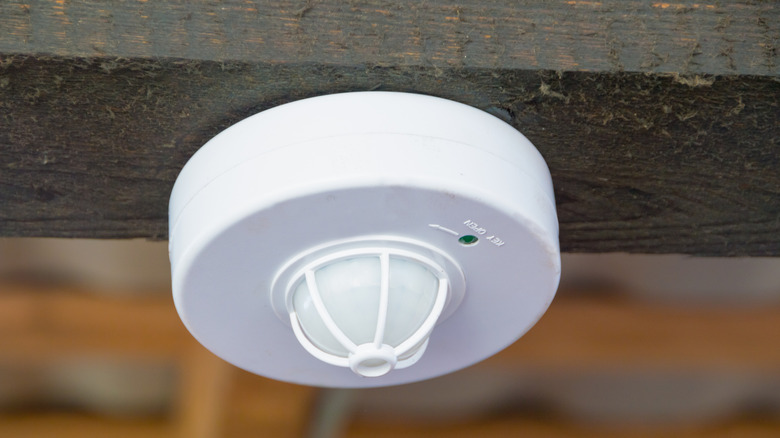A smoke detector on a ceiling with green light lit up.