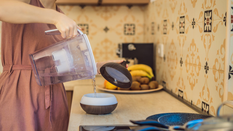 A person pouring filtered water into a diffuser or humidifier