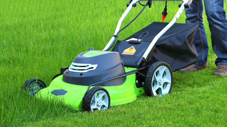 A person pushing a lawn mower through tall grass