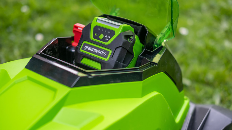A close-up of a lawn mower with a focus on the battery labeled 
