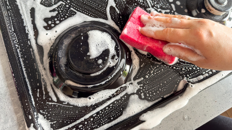 Hand cleaning gas stove with sponge and soap
