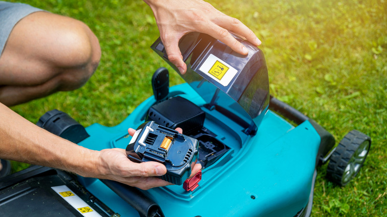 A person placing a battery into a blue electric lawn mower
