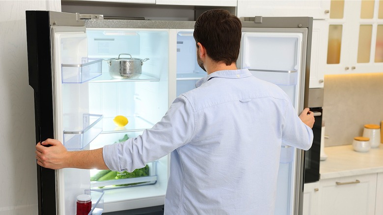 Person holding a near-empty refrigerator's double doors open