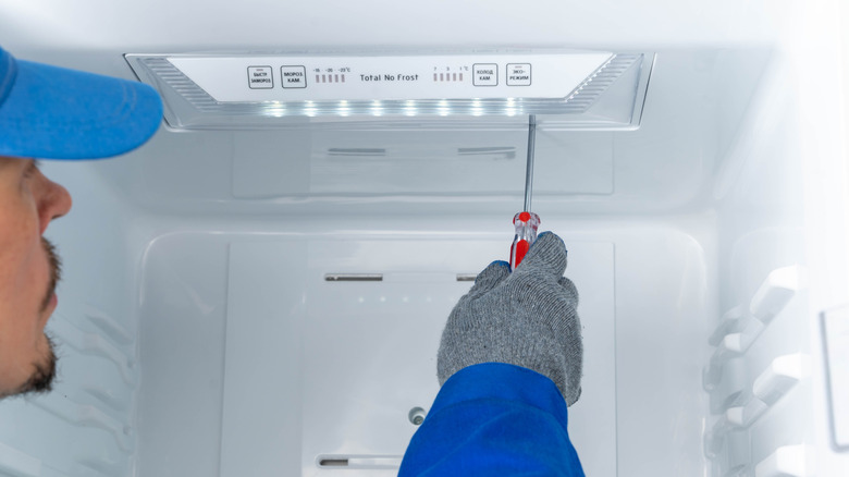 A repair worker using a screwdriver on the inside of a refrigerator
