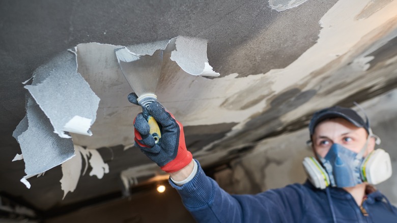 Person scraping paint off ceiling