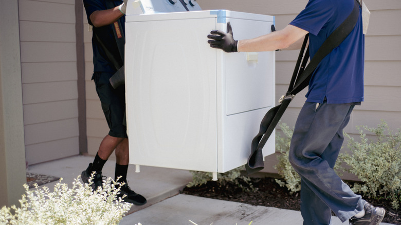 Two movers carrying an old dryer from a house.