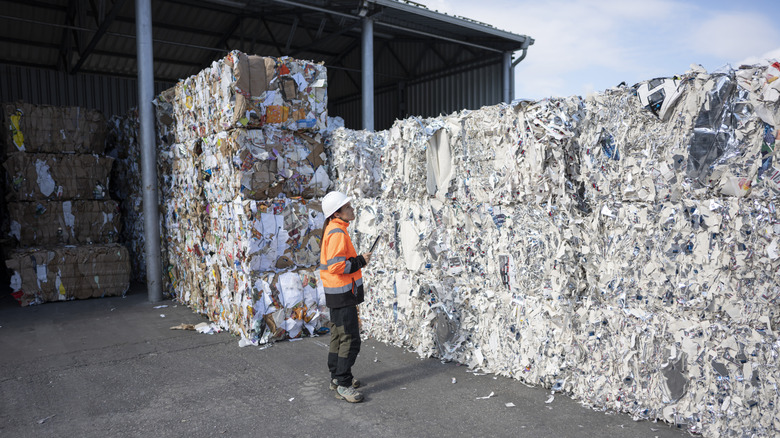 A person in an orange safety vest and a hard hat looking at bales of recycling