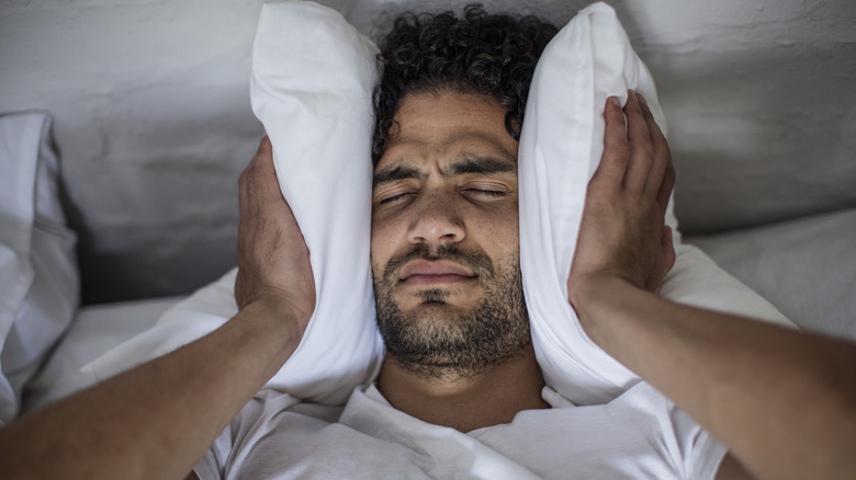 Man trying to block sound with bed pillow