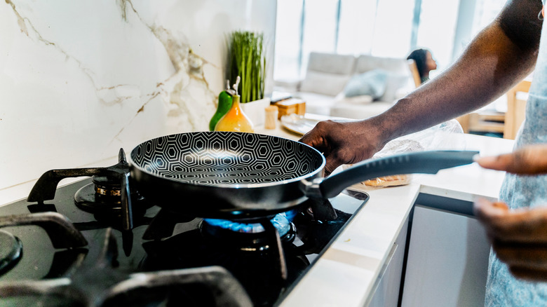 A man adjusting the flame on a gas stove with a pan on the burner