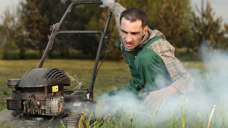 Man looks concerned at smoking lawn mower