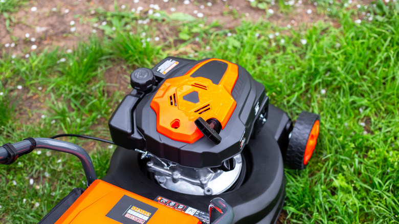 An orange and black lawn mower cutting grass.