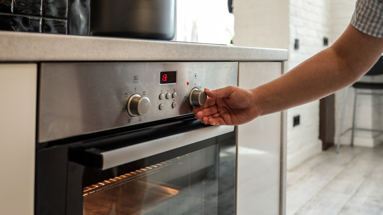 A person adjusting a chrome oven front with a black door below it.