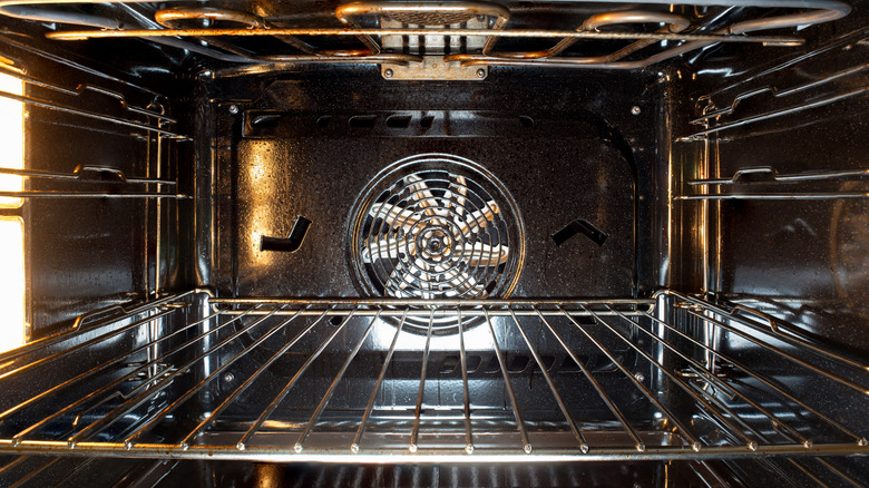The inside of an oven with a chrome rack and a view of the fan at the back of it.